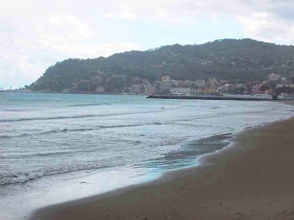 Waves on sandy beach, village on pier beneath green hills