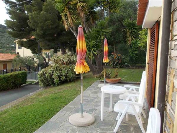 Terrace with white chairs and table, closed umbrellas among yuccas and hedges