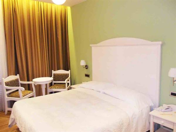 Hotel room with white bed, white headboard, green wall and gold curtains