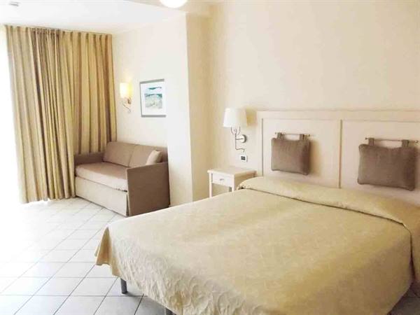 Hotel room with double bed, beige sofa and light curtains