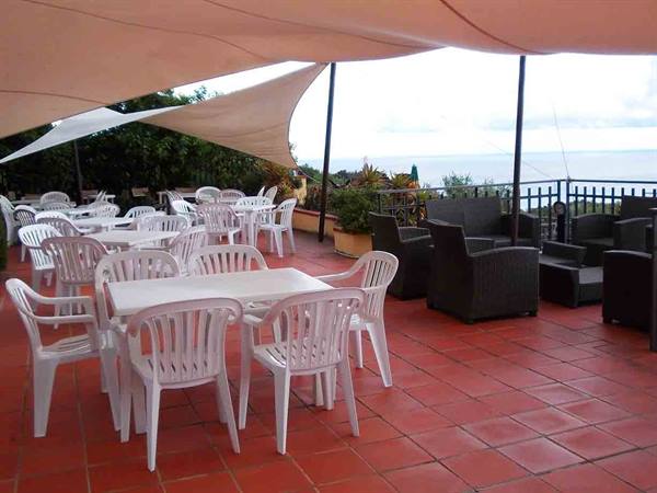 Terrace with white plastic tables and chairs under shade sails facing the sea
