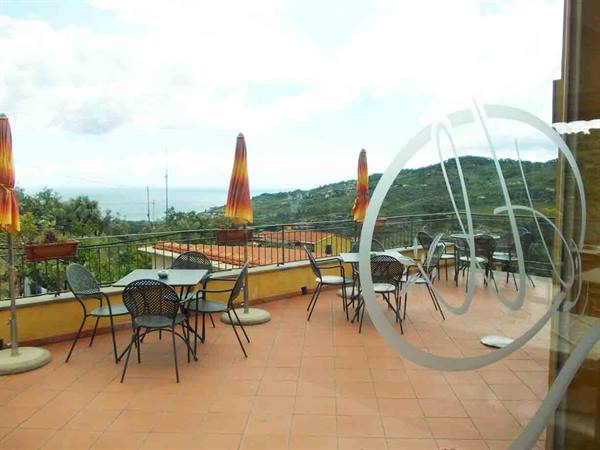 Terrace with iron tables and chairs, closed umbrellas, hills and sea in the background