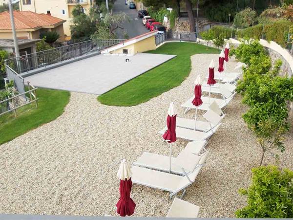 White sun loungers and closed red umbrellas on gravel, paddle courts and houses