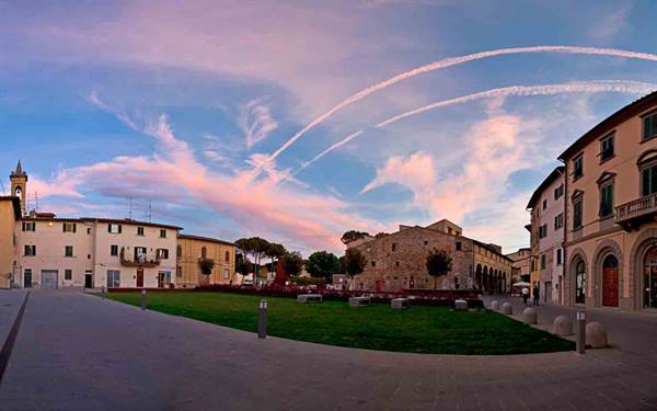 Town square with green lawn, stone buildings and pink sky streaked with contrails