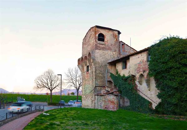 Old medieval stone tower with machicolations, ivy-covered walls and passing cars