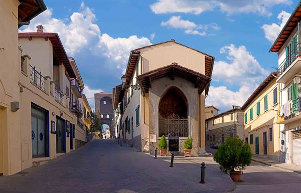 Small church with open archway on cobbled street among houses in Lastra a Signa