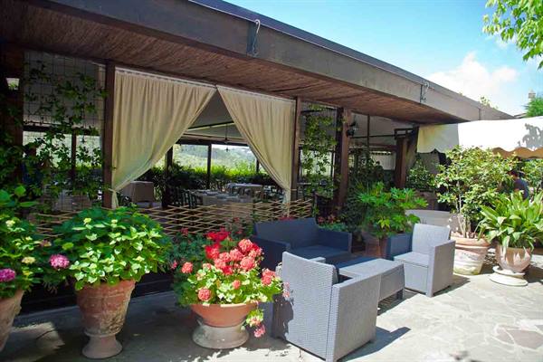 Restaurant terrace with grey armchairs, beige curtains and flower pots