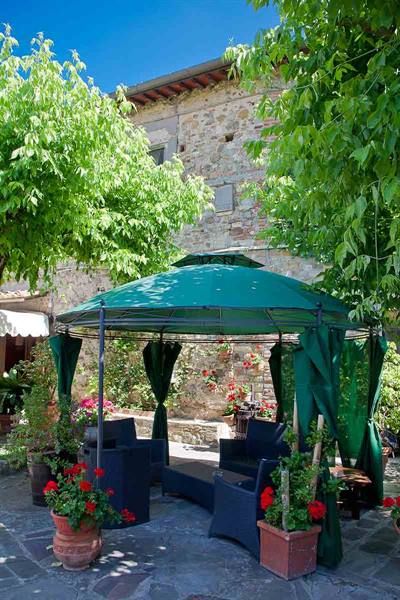 Green gazebo with dark sofas in a stone courtyard, red geranium pots