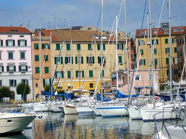 Sailboat masts in the harbor before colorful buildings with green shutters