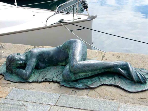 Bronze statue of a reclining woman on the dock, moored boats behind