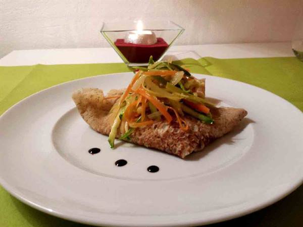 Buckwheat crêpe with julienned vegetables on white plate, lit candle
