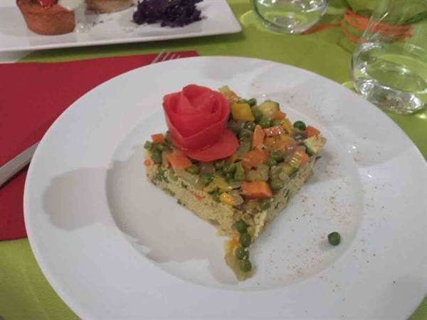 Vegetable flan with peas and carrots, garnished with a tomato rose, white plate