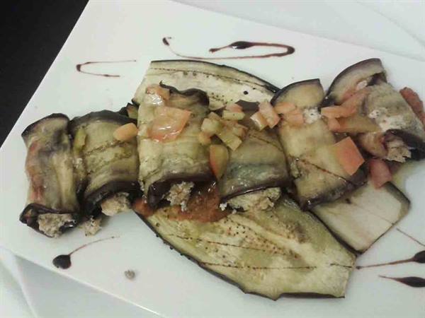 Stuffed eggplant rolls drizzled with sauce on a white plate