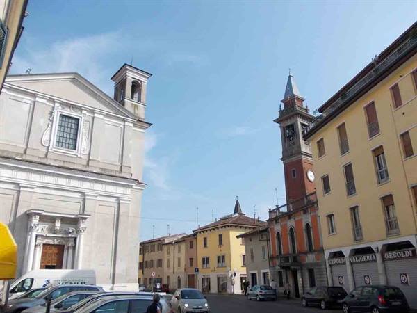 Square with white church and red clock bell tower, parked cars under blue sky