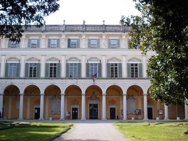 Arcaded facade with green-shuttered windows, entrance framed by trees