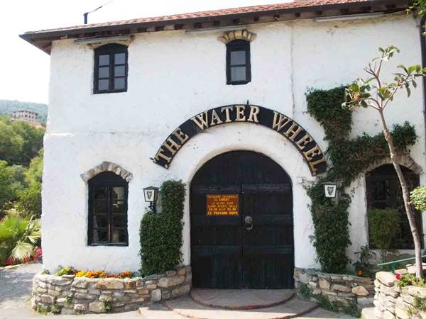 Black arched entrance with The Water Wheel sign on white building surrounded by greenery