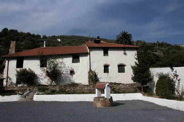 White rural house with red roof and stone well in front