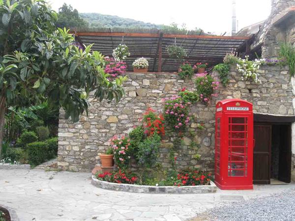 Red telephone booth against a stone wall with flowers and pergola