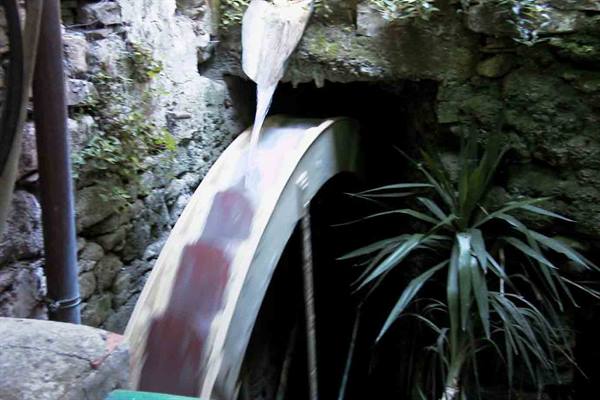 Water flowing over a wooden mill wheel beside stone walls