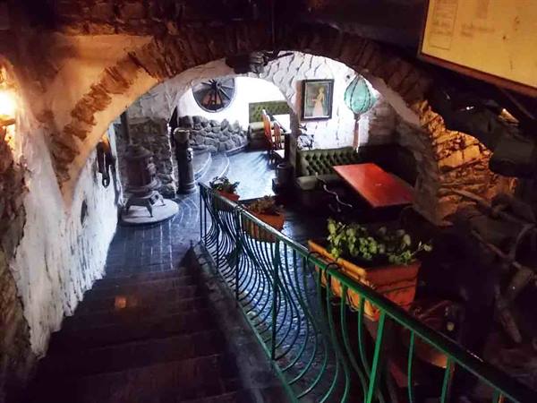 Rustic stone interior with arch, wood stove, tables and green railing