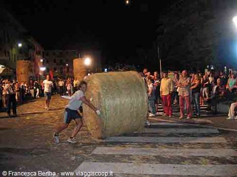 Man pushes a large straw roll along the street at night, crowd watching