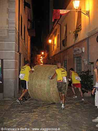 Men push a giant hay bale through a lantern-lit narrow alley at night