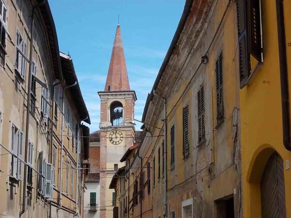 Bell tower with clock between ochre houses, blue sky