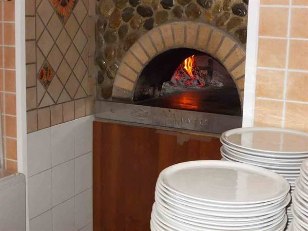 Wood-fired brick oven burning, stacks of white plates in front