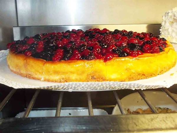 Berry cheesecake topped with raspberries and currants, displayed in a chilled case