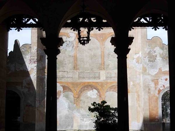 Dark columns silhouetted against a faded frescoed courtyard with a green plant