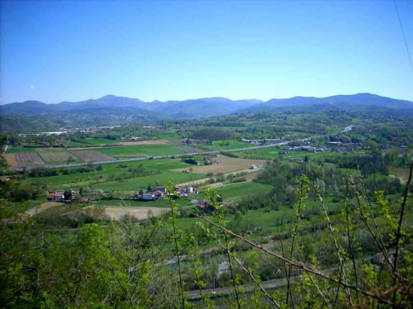 Green valley with farmed fields, highway and Apennine hills under clear blue sky