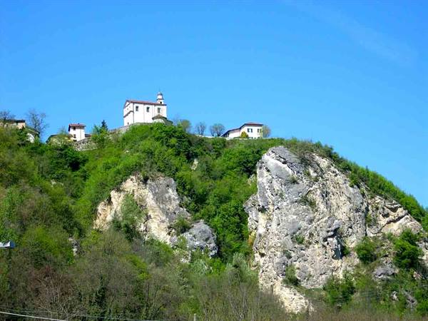 Church with bell tower atop rocky green hill under blue sky