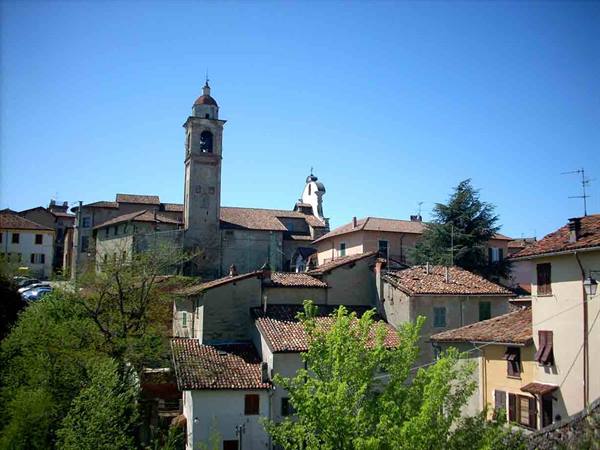 Hillside village with terracotta-roofed houses and tall bell tower under blue sky