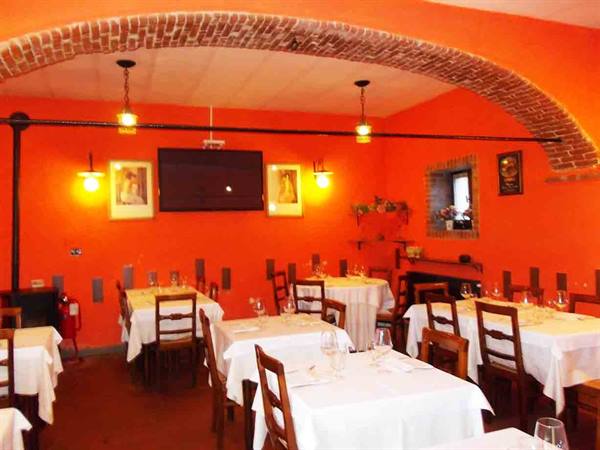 Restaurant dining room with orange walls, brick arch, white-clothed set tables