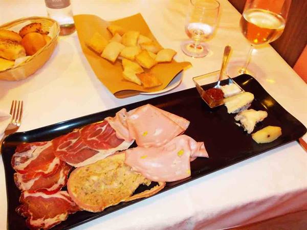 Black tray with cured meats, cheeses and fried dough, glass of white wine