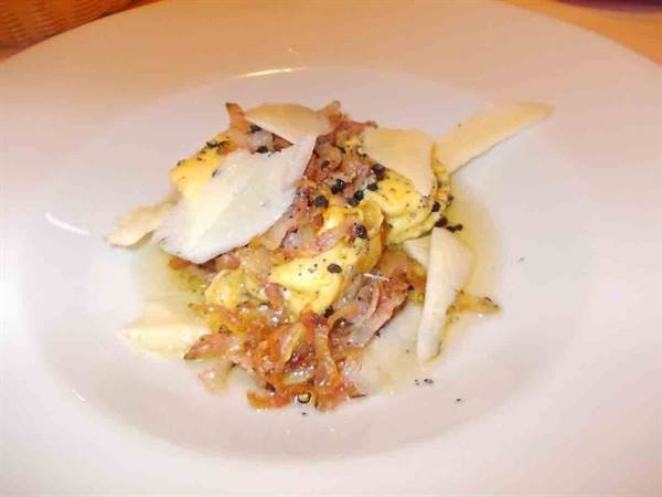 White plate with truffle ravioli, crispy bacon and parmesan shavings