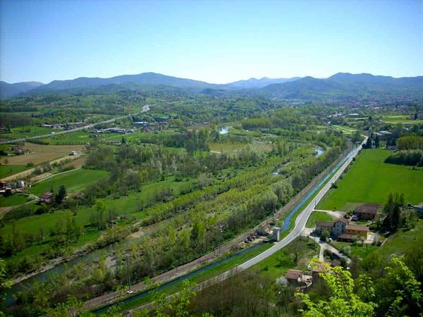 River, road and green fields among hills and scattered houses under blue sky
