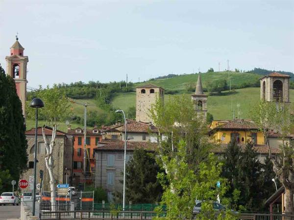 Bell towers and medieval brick buildings among green hills in background