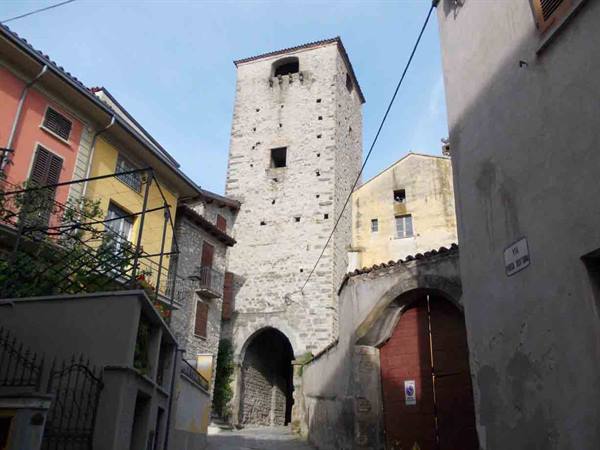 Ancient medieval stone tower with arched gateway among old village houses