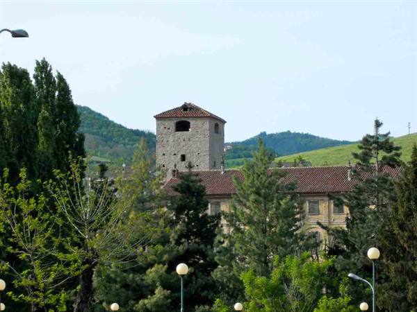 Old stone tower with tiled roof above buildings among green trees and hills