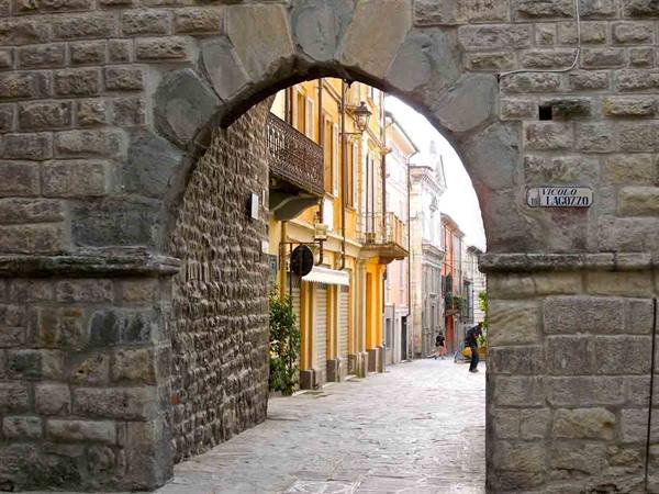 Stone archway opening onto cobbled alley with colorful houses and Via Volta sign