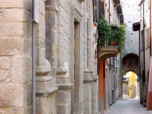 Narrow stone alley with flowered balcony and medieval arch, San Marino