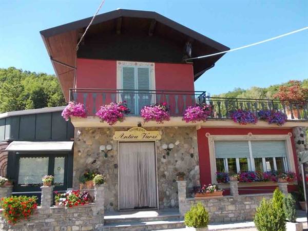 Stone-and-red Trattoria Fiori with pink geraniums on balcony, green hills