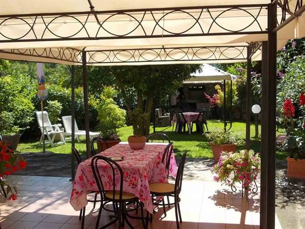 Table with pink tablecloth under wrought iron gazebo, chairs and flowers in garden