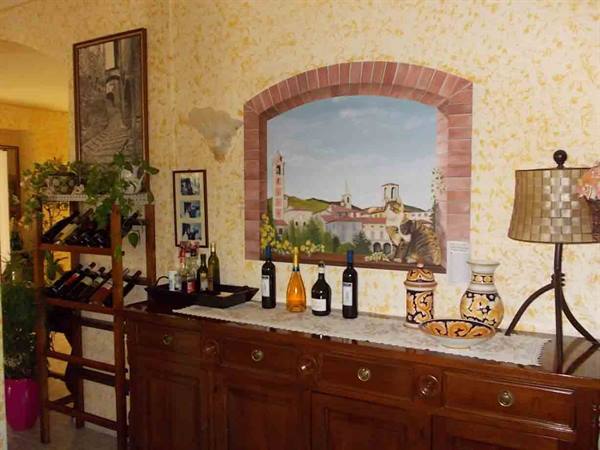 Wine bottles on wooden sideboard beneath brick-arched mural in warm lamplight