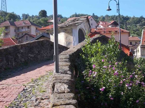 Stone bridge with chapel, pink flowers and red roofs in the village