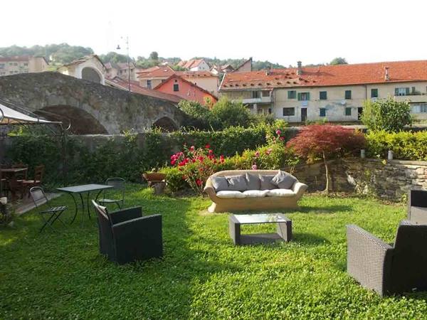 Garden with rattan sofa and armchairs on the lawn, behind a stone bridge and red-roofed houses