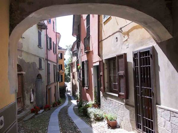 Cobbled uphill alley between colorful houses seen through an arch, flowers on steps