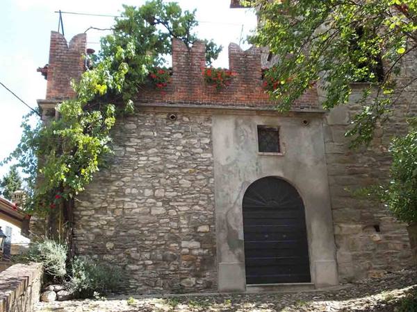 Stone wall with brick battlements, dark arched doorway and climbing roses