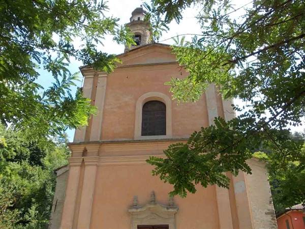 Pink church facade with bell tower, framed by green leafy trees